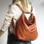 Image shows a model wearing a supple, slouchy tan backpack. 